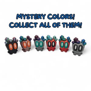 May include: Six colourful figurines with crystal-like headpieces and round eyes are displayed. The figurines are in various colours, including black, orange, grey, and red. The text "MYSTERY COLORS! COLLECT ALL OF THEM!" is above the figurines.