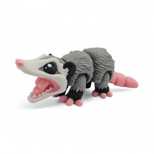 May include: A gray and white opossum figurine with a pink nose, mouth, and tail. The opossum has black ears and feet, and its mouth is open, revealing teeth and a pink tongue. The figurine is on a white background.