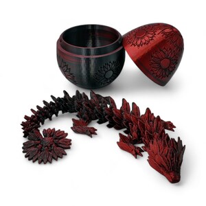 Puede incluir: Un drag&oacute;n rojo y negro impreso en 3D hecho de piezas que encajan. El drag&oacute;n est&aacute; enroscado y tiene un dise&ntilde;o de girasol en sus escamas. El drag&oacute;n viene en un contenedor en forma de huevo rojo y negro con un dise&ntilde;o de girasol.
