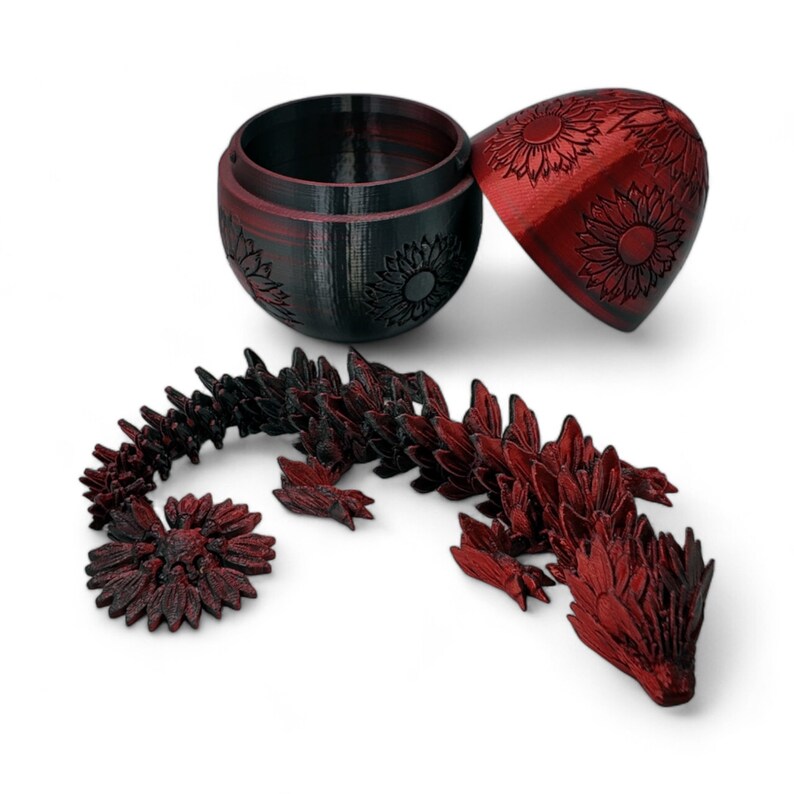 Puede incluir: Un drag&oacute;n rojo y negro impreso en 3D hecho de piezas que encajan. El drag&oacute;n est&aacute; enroscado y tiene un dise&ntilde;o de girasol en sus escamas. El drag&oacute;n viene en un contenedor en forma de huevo rojo y negro con un dise&ntilde;o de girasol.