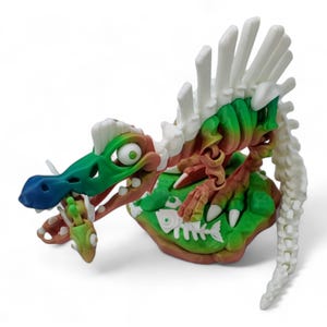 May include: A green, white, and red skeleton dinosaur toy with a blue nose and a white spine. The dinosaur is holding a fish in its mouth and is standing on a green and brown base.