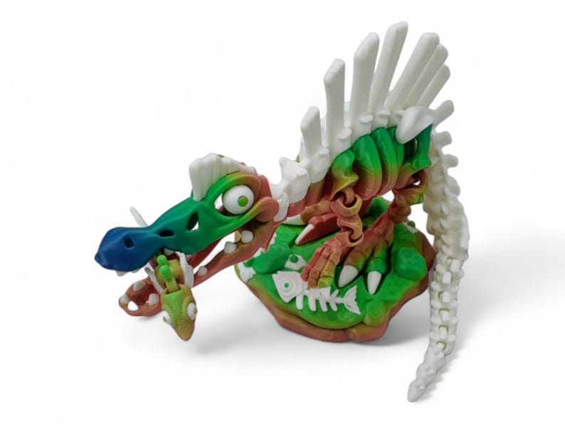 May include: A green, white, and red skeleton dinosaur toy with a blue nose and a white spine. The dinosaur is holding a fish in its mouth and is standing on a green and brown base.