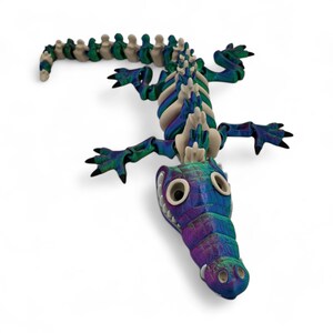 Pu&ograve; includere: Una scultura di alligatore colorata e stilizzata con un design scheletrico dettagliato. L'alligatore presenta un vivace mix di tonalit&agrave; blu, verdi e viola, con una spina dorsale color crema. Le sue zampe e la coda sono allungate e gli occhi sono grandi e rotondi.