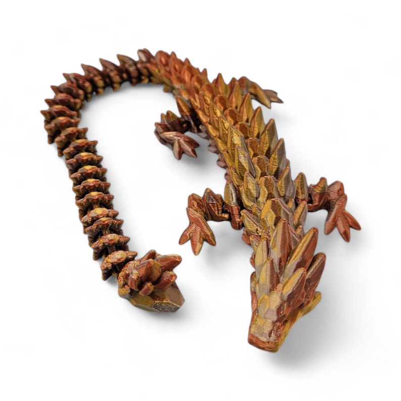 May include: A 3D printed golden lizard with a textured, scaly surface. The lizard is posed with its tail curled up and its head tilted slightly upwards.