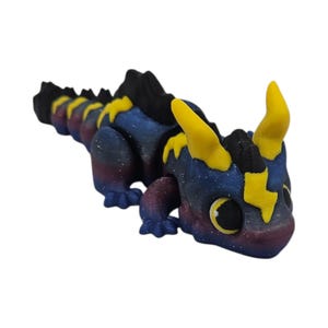 K&ouml;nnte beinhalten: Eine 3D-gedruckte Drachenfigur im Galaxien-Design. Der Drache hat einen dunkelblauen K&ouml;rper mit lila und wei&szlig;en Sprenkeln, gelben Blitzakzenten und gelben H&ouml;rnern. Der Drachenr&uuml;cken und -kopf sind schwarz.