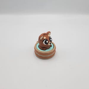 May include: A brown clay figurine of a dog with large eyes, sitting in a light blue and brown tub. The dog has white markings on its ears and face. The tub has a light blue interior and brown exterior.