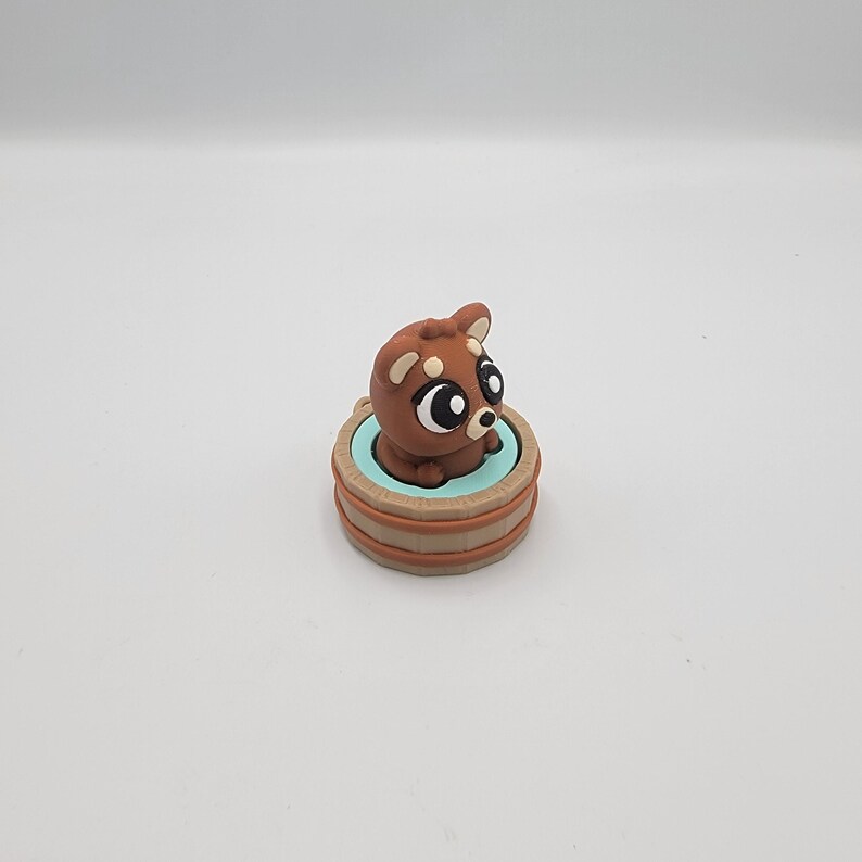 May include: A brown clay figurine of a dog with large eyes, sitting in a light blue and brown tub. The dog has white markings on its ears and face. The tub has a light blue interior and brown exterior.