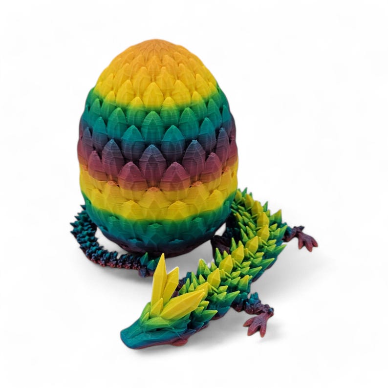 May include: A 3D-printed dragon and egg set. The egg is a vibrant rainbow of colors, with a textured, layered design. The dragon is green, yellow, and blue, with a spiky spine and tail. The dragon is lying down next to the egg.