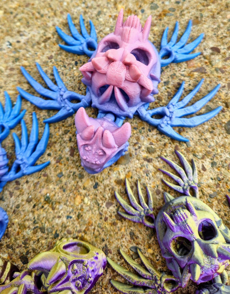 Peut inclure: Trois figurines squelettiques imprim&eacute;es en 3D avec des ailes. Les figurines sont dans des tons de violet, bleu et or. Les figurines sont pos&eacute;es dans diff&eacute;rentes positions.