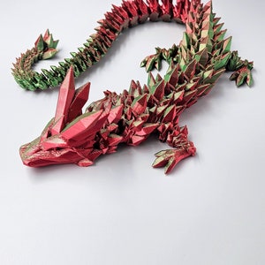May include: A 3D printed dragon figurine with a red and green iridescent finish. The dragon is posed in a crawling position with its head raised and its tail curled.