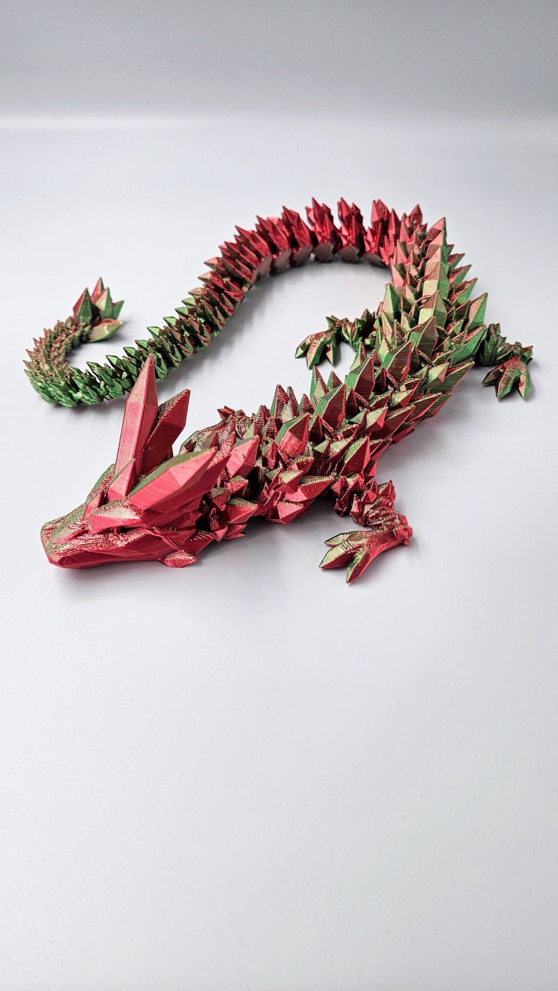 May include: A 3D printed dragon figurine with a red and green iridescent finish. The dragon is posed in a crawling position with its head raised and its tail curled.