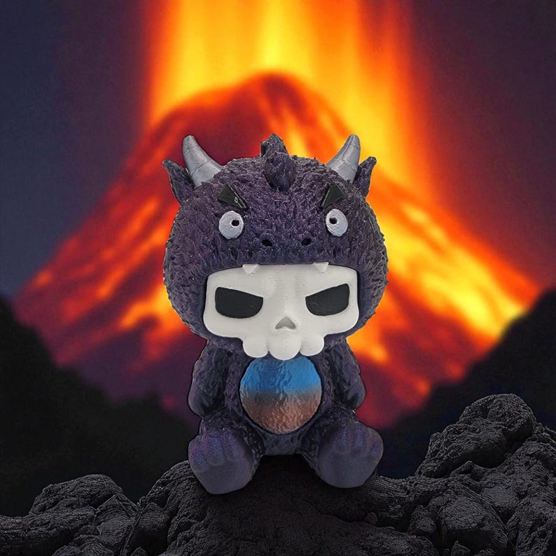 Puede incluir: Un juguete de monstruo de peluche morado con una cara en forma de calavera y peque&ntilde;os cuernos. El juguete tiene una barriga azul y marr&oacute;n y est&aacute; sentado sobre una superficie oscura y rocosa. El fondo presenta un volc&aacute;n en llamas.