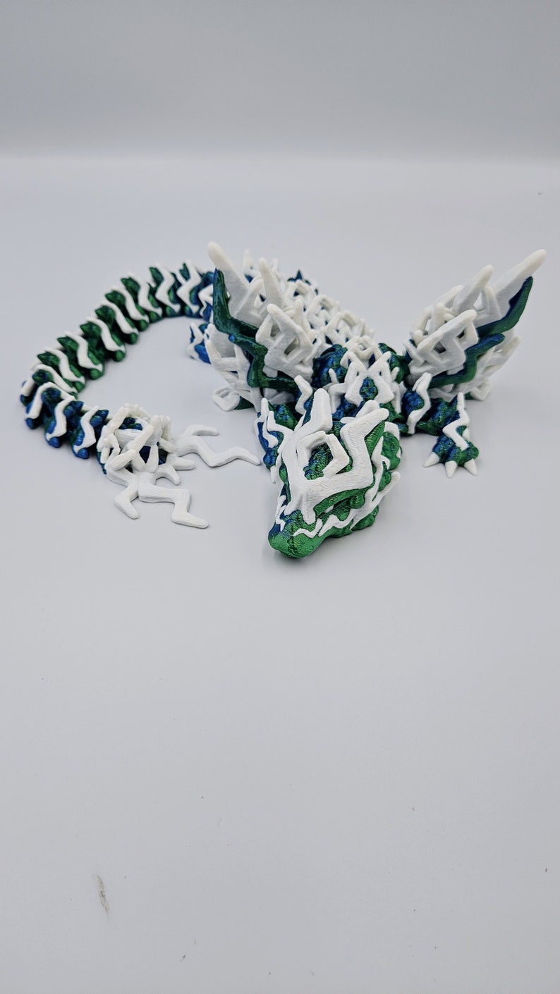 May include: A 3D printed dragon figurine with a white and green colour scheme. The dragon has a long, segmented tail and a detailed head with sharp teeth.
