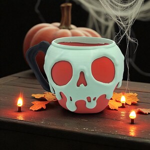 Pode incluir: Uma caneca vermelha e branca em forma de caveira com uma al&ccedil;a preta, perfeita para o Halloween. A caneca tem um design verde claro e gotejante em torno das caracter&iacute;sticas da caveira. A caneca est&aacute; em uma superf&iacute;cie de madeira com folhas de outono e pequenas velas.