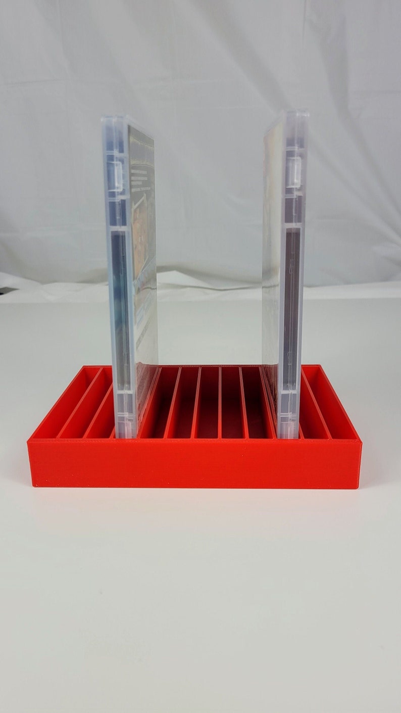 May include: Red plastic DVD storage case with two clear plastic DVD cases standing upright in the slots.