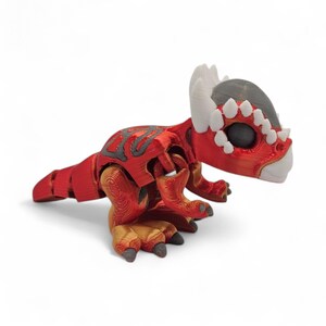 May include: A red and gray 3D-printed dinosaur toy with a detailed design. The toy features a segmented body, horns, and a textured surface. The dinosaur is posed on a white background.
