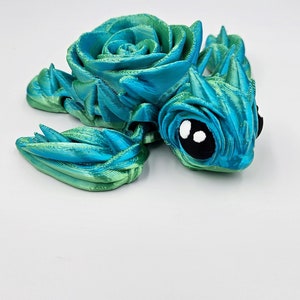 May include: A 3D printed blue and green turtle figurine with a rose-shaped shell. The turtle has large black eyes with white pupils.