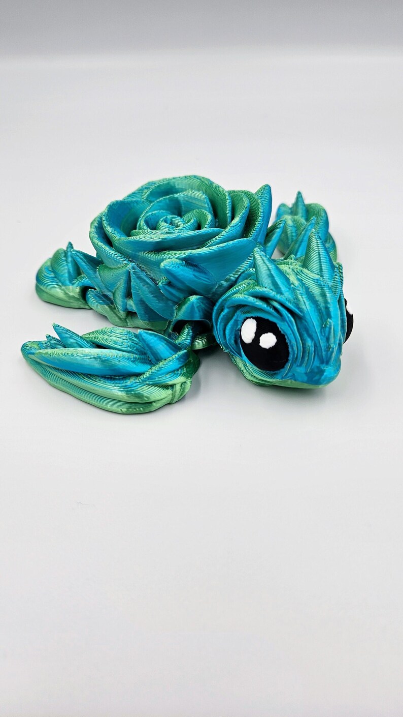 May include: A 3D printed blue and green turtle figurine with a rose-shaped shell. The turtle has large black eyes with white pupils.