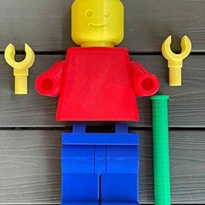 K&ouml;nnte beinhalten: Eine gro&szlig;e, farbenfrohe Lego-Figur mit gelbem Kopf, rotem Torso und blauen Beinen. Zwei gelbe schraubenschl&uuml;sself&ouml;rmige Zubeh&ouml;rteile und ein gr&uuml;ner Zylinder sind in der N&auml;he der Figur platziert. Die Figur ist ein lustiges, &uuml;bergro&szlig;es Spielzeug.