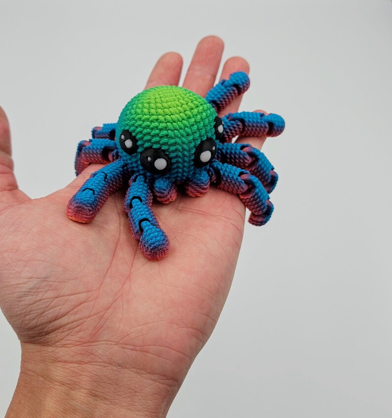 Op de afbeelding: Een klein, gehaakt octopus speelgoed met een groene, blauwe en roze gradi&euml;nt. De octopus heeft grote, zwarte ogen en acht tentakels.