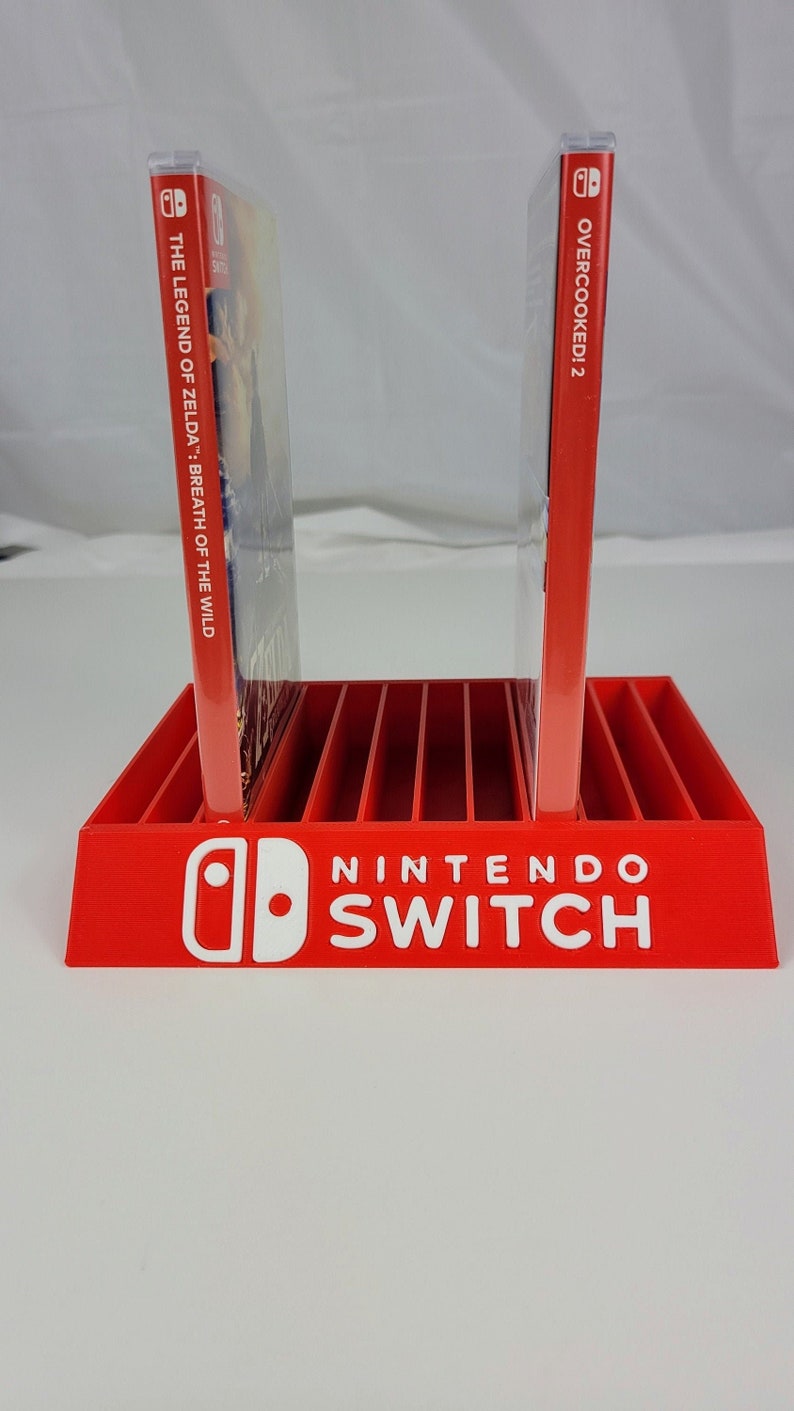 May include: Red plastic Nintendo Switch game case holder with slots for multiple games. The holder has the Nintendo Switch logo on the front. Two game cases are in the holder, one for "The Legend of Zelda: Breath of the Wild" and one for "Overcooked! 2".
