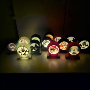 May include: A collection of illuminated, spherical decorative lights with various holiday-themed designs. The lights feature images of Santa Claus, pumpkins, and winter scenes. Each light sits on a small, wooden base, creating a warm, inviting glow.