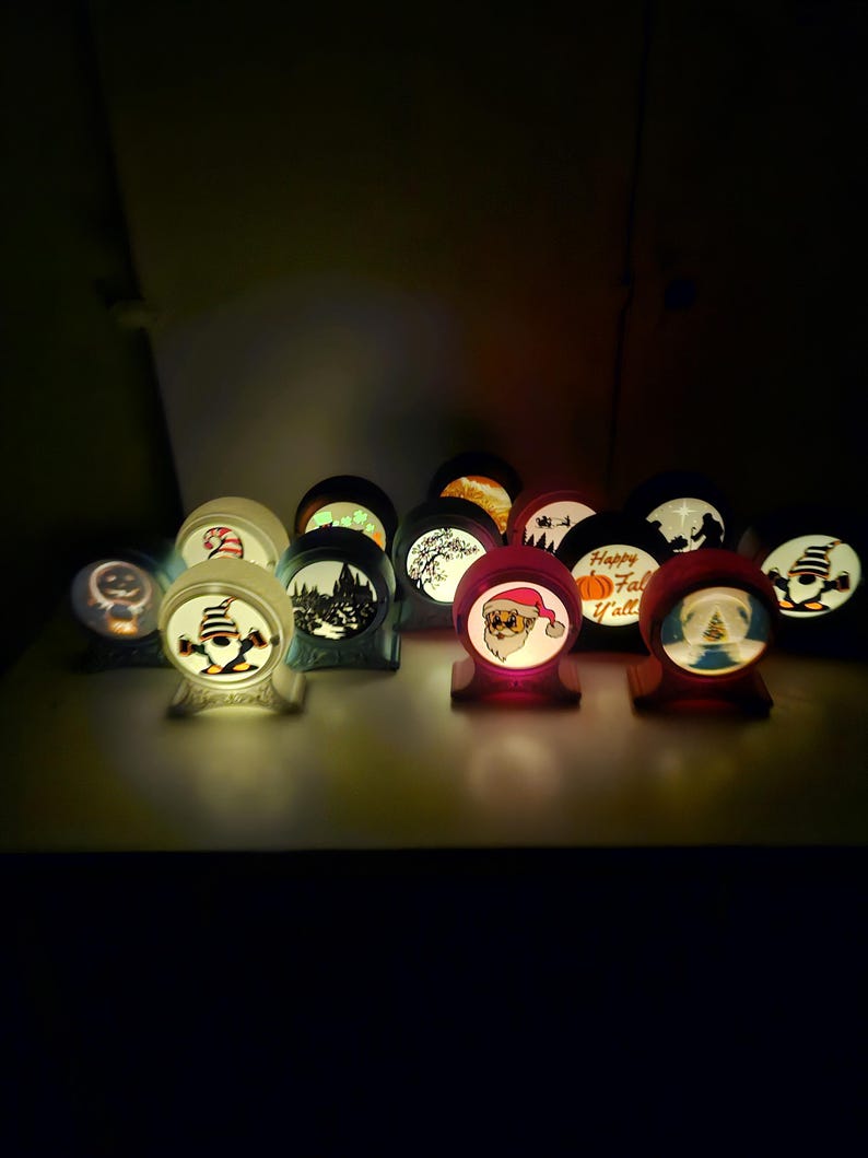 May include: A collection of illuminated, spherical decorative lights with various holiday-themed designs. The lights feature images of Santa Claus, pumpkins, and winter scenes. Each light sits on a small, wooden base, creating a warm, inviting glow.