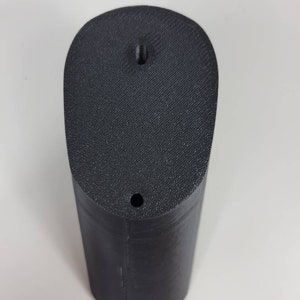 May include: A black plastic 3D printed object with a rounded top and a hole in the center. The object has a smooth, textured surface.