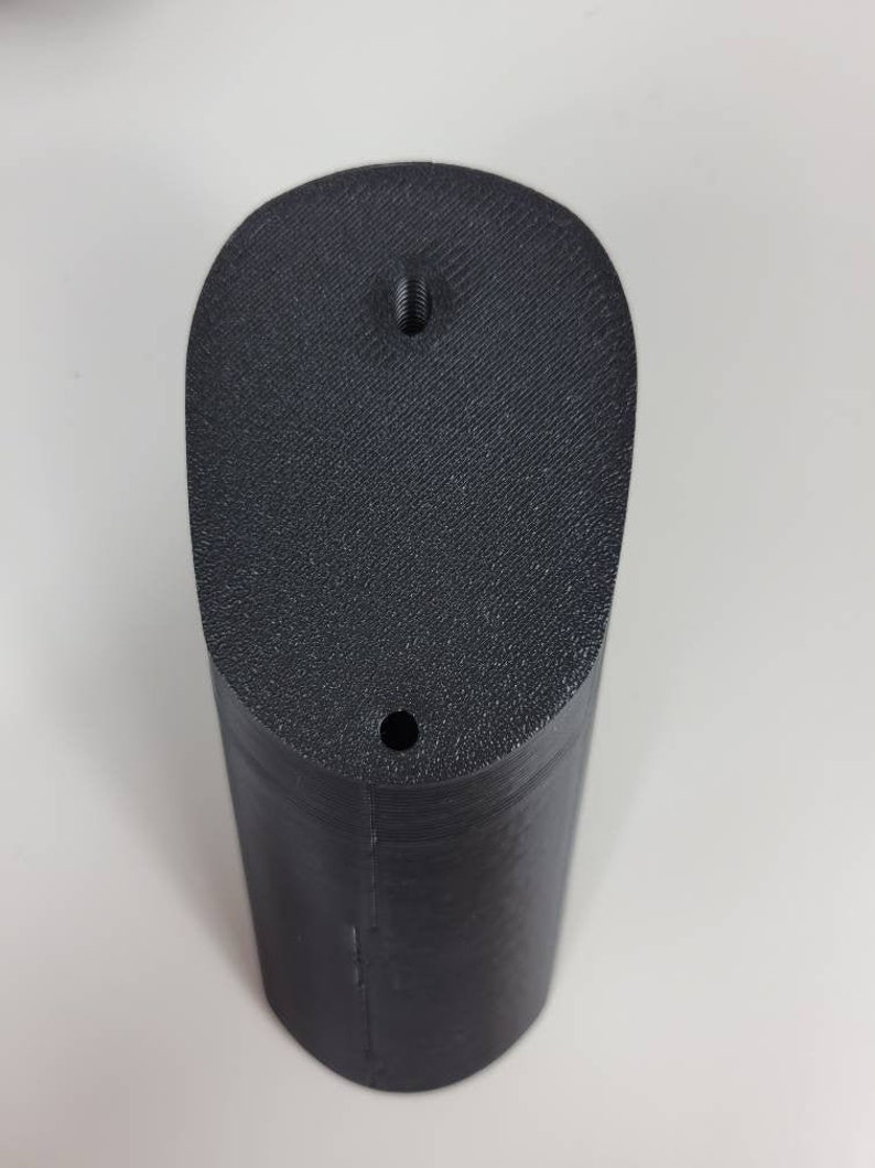 May include: A black plastic 3D printed object with a rounded top and a hole in the center. The object has a smooth, textured surface.