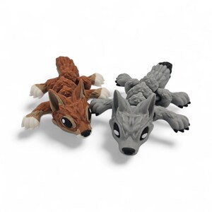 Peut inclure: Deux figurines d'animaux jouets : un &eacute;cureuil brun et un loup gris. L'&eacute;cureuil a un corps textur&eacute;, des pattes blanches et un visage d&eacute;taill&eacute;. Le loup a un design similaire, avec un nez et des oreilles noirs. Les deux sont couch&eacute;s.