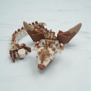 以下が含まれることがあります： 茶色とオフホワイトの様々な色合いで作られた、ドラゴンの詳細な彫刻。 ドラゴンは、長くセグメント化された体、大きな翼、詳細な頭部が特徴です。 彫刻は無地の背景に設定されています。