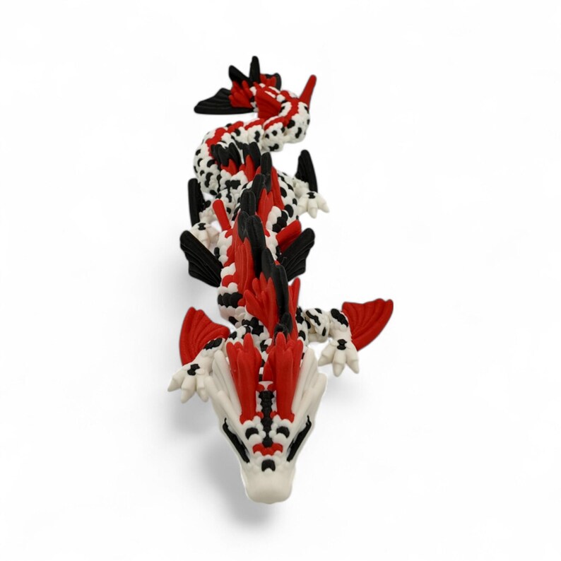 May include: A detailed, top-down view of a dragon figurine. The dragon is white with black spots and red accents on its fins and head. The dragon's head is white with black details. The figurine is set against a plain white background.