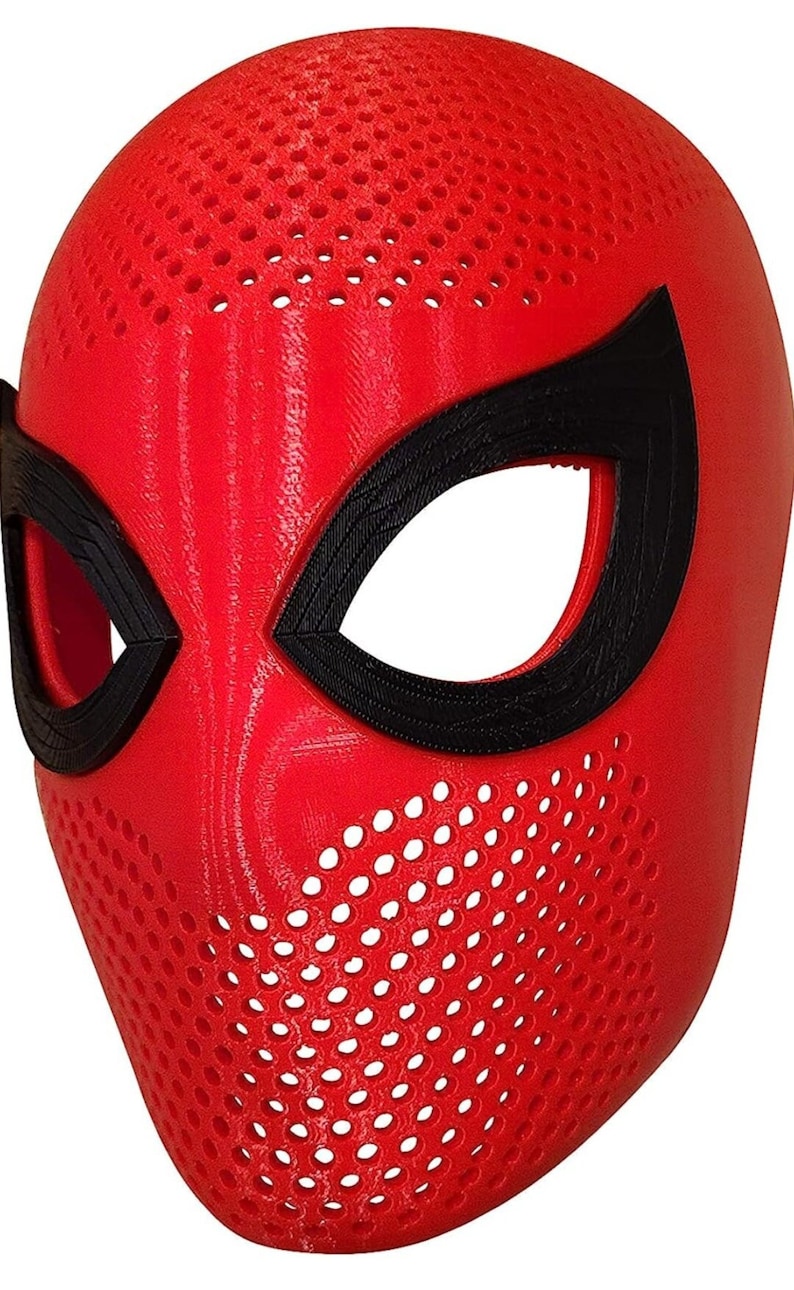 May include: A red mask with black eye surrounds, featuring a perforated design across the surface. The mask is a full face covering, likely for costume or cosplay purposes. The eye openings are large and oval-shaped.