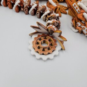 May include: A white and gold gear with a white and gold leaf design. The gear is made of plastic and has a detailed design.