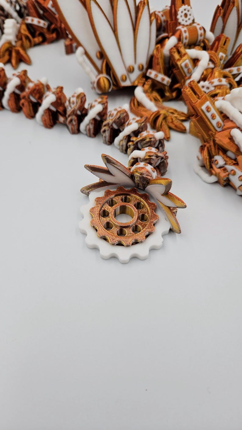May include: A white and gold gear with a white and gold leaf design. The gear is made of plastic and has a detailed design.