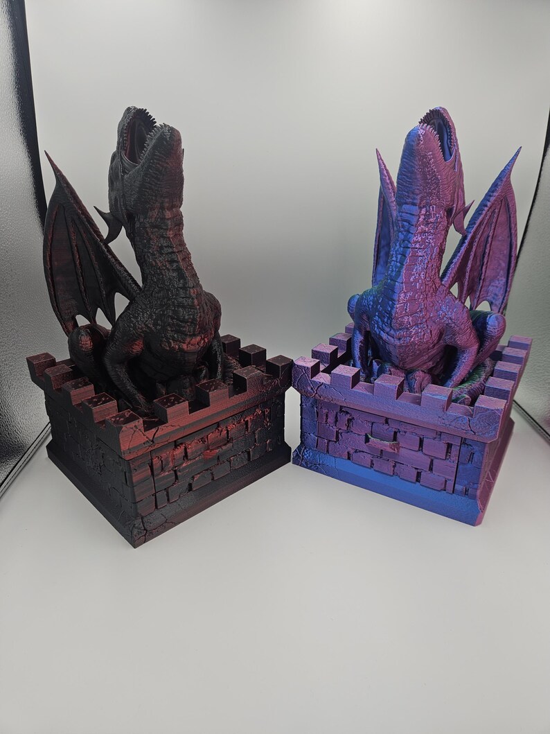 May include: Two dragon sculptures, one black and red, the other blue and purple. Each dragon is perched atop a castle-like structure with open mouths and outstretched wings. The sculptures are detailed and have a fantasy theme.