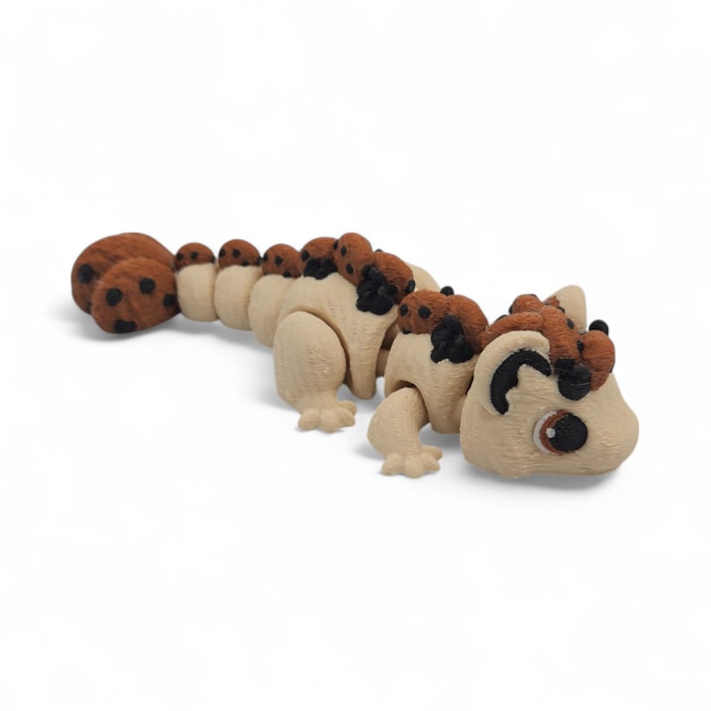 May include: An articulated toy caterpillar with a light tan body and brown detailing. The toy's segments are connected, allowing for flexible posing. The caterpillar has a detailed face and is designed to resemble a friendly creature. The toy is made of wood.