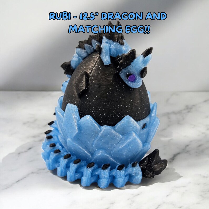 May include: A 12.5 inch black and blue dragon figurine with glitter details. The dragon is curled up inside a blue egg with a crystal-like texture. The text "RUBI - 12.5" DRAGON AND MATCHING EGG!!" is written in white on a black background above the figurine.