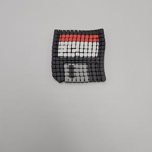May include: A pixelated floppy disk design in black, red, and white. The square-shaped disk has a grid-like pattern, with a red top border and a white and black center. The design is on a plain white background.