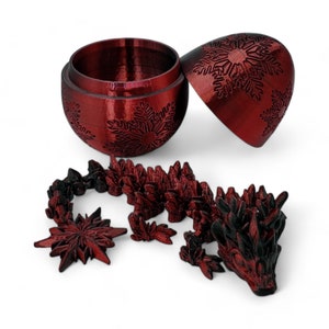 K&ouml;nnte beinhalten: Ein roter, detailreich gestalteter, 3D-gedruckter Weihnachtsanh&auml;nger in Form einer Schneeflocke. Der Anh&auml;nger ist ge&ouml;ffnet und zeigt einen hohlen Innenraum. Eine kleinere, rote, 3D-gedruckte Drachenfigur ist ebenfalls abgebildet.