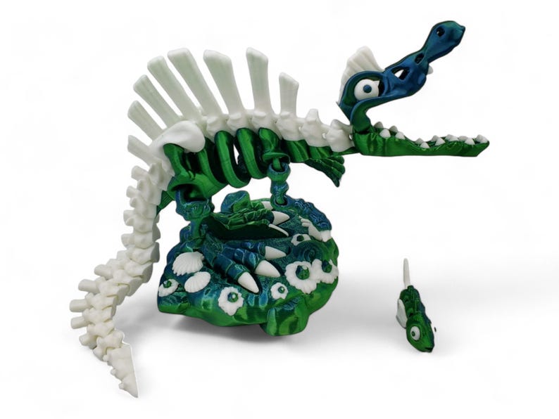 May include: A green and white skeletal dinosaur toy with a blue head and large eyes. The dinosaur is standing on a green and blue base with white eyes. A smaller green and white fish toy is in the foreground.