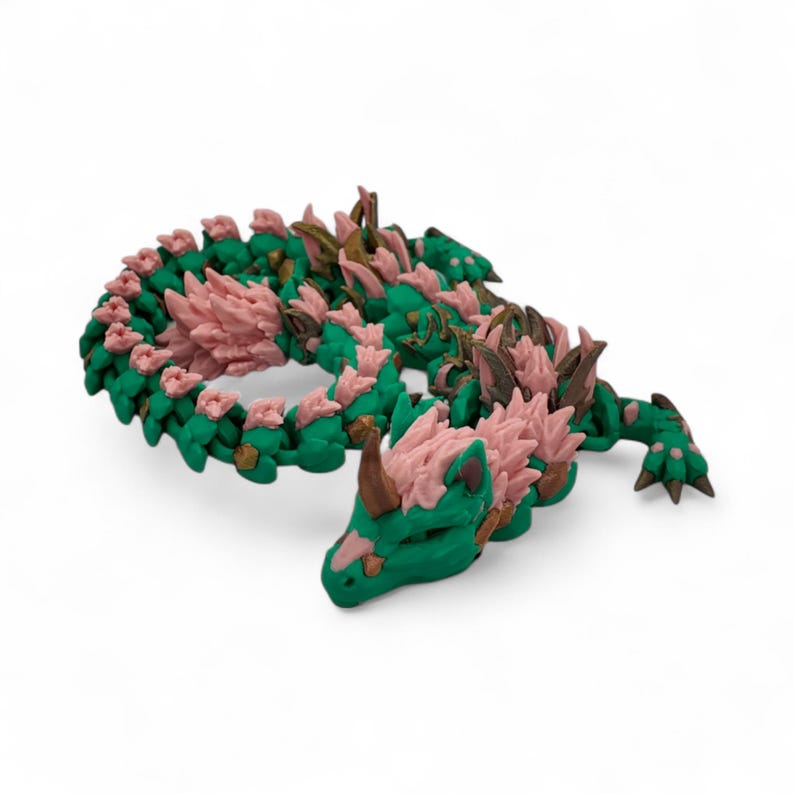 May include: A green and pink dragon figurine with a detailed design. The dragon has a long, winding body with pink accents along its back and head. The dragon's horns and claws are a darker brown color.