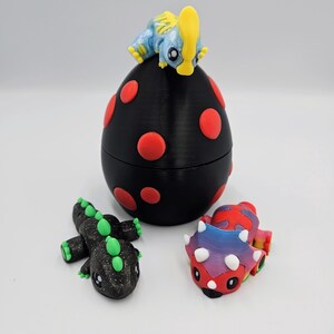 May include: Three small dinosaur figurines, one on top of a black egg with red polka dots, one black with green accents, and one multi-colored with white horns.