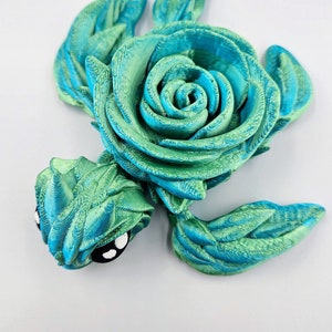 May include: A 3D printed sea turtle figurine with a green and blue swirl pattern. The turtle's shell is shaped like a rose.