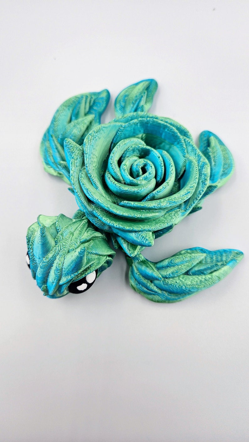 May include: A 3D printed sea turtle figurine with a green and blue swirl pattern. The turtle's shell is shaped like a rose.