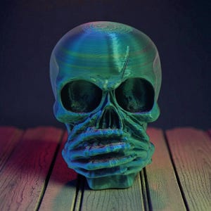 Op de afbeelding: Een teal en blauwe schedelsculptuur met een getextureerd oppervlak. De schedel heeft grote oogkassen, een prominente neus en een gedetailleerde kaaklijn. De sculptuur staat op een houten oppervlak.