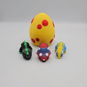 May include: A yellow egg with red spots, and three small dinosaur figurines. The dinosaurs are black, blue, and red and purple.