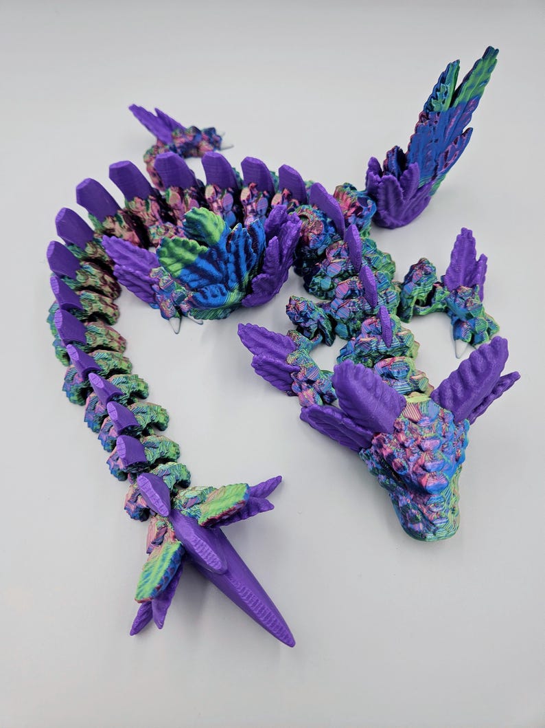 May include: A 3D printed dragon figurine with a purple and iridescent finish. The dragon is curled up in a coil with its head raised and its wings spread out. The dragon's scales are detailed and textured.