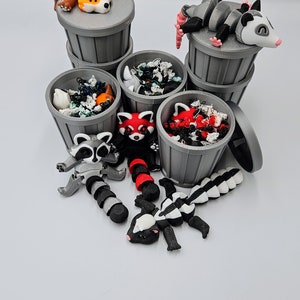 May include: A collection of miniature gray trash cans, each filled with colorful debris and topped with various animal figurines. The animals include a fox, opossum, raccoon, red panda, and skunk. The figurines are in various poses.