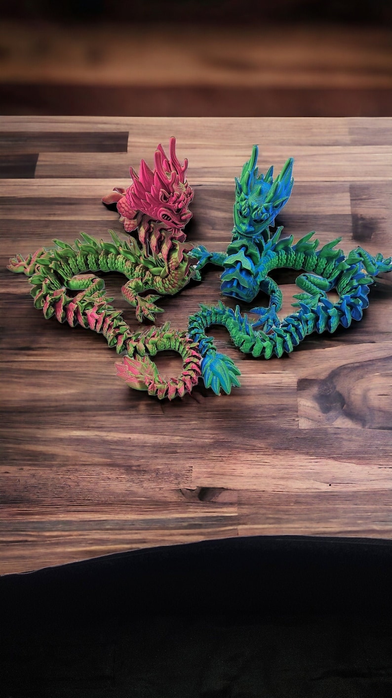 May include: Four articulated dragon figurines in vibrant colors: pink, green, and blue. The dragons are posed on a wooden surface, showcasing their detailed, scaled bodies and spiky features. These decorative figurines are a unique addition to any collection.